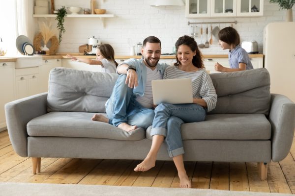 Happy,Parents,Using,Laptop,,Sitting,On,Couch,While,Kids,Playing