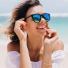 Wonderful woman in white attire and sparkle glasses posing with happy face expression in hot summer day. Pleasant caucasian girl standing near ocean on sky background..