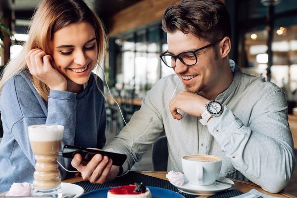 Happy couple watching a movie on smartphone, enjoying resting time at cafe