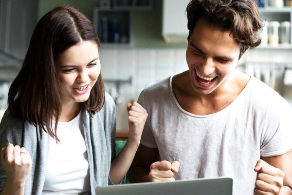 Excited couple ecstatic by online win looking at laptop screen