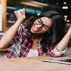 Wonderful female student sitting in cafe with laptop and laughin