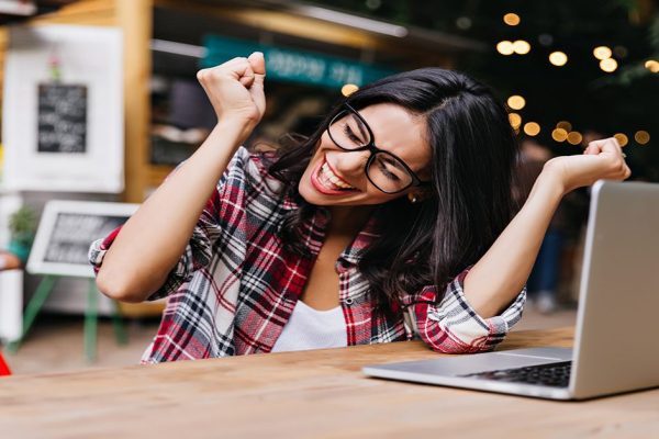 Wonderful female student sitting in cafe with laptop and laughin