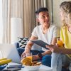 young couple sitting on sofa at home working online on laptop and tablet, using internet, smiling, happy together, having fun, man and woman in love, family leisure time, having breakfast in morning