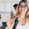 Close-up portrait of pretty female manager from sales department. Indoor photo of smiling girl working in office with discussing people on background..